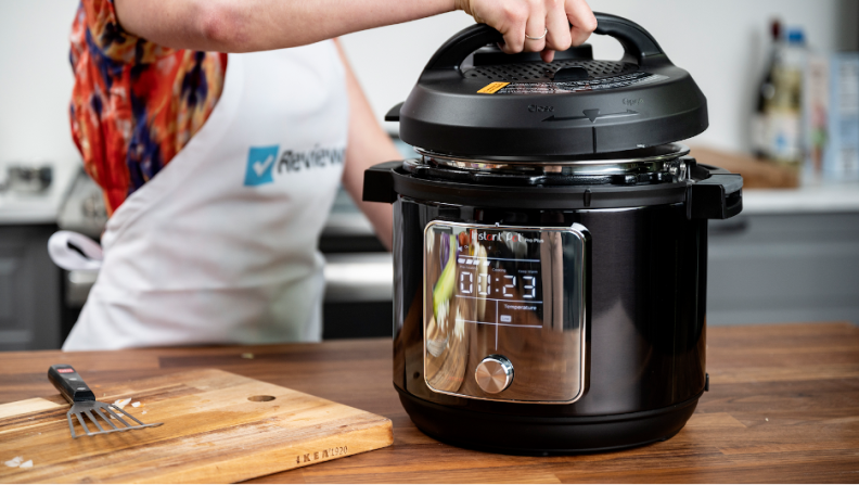 A woman wearing a Reviewed apron lifting the lid off of an Instant Pot Pro.
