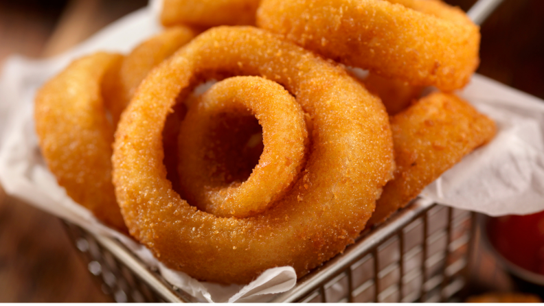 A frying basket full of fresh onion rings.