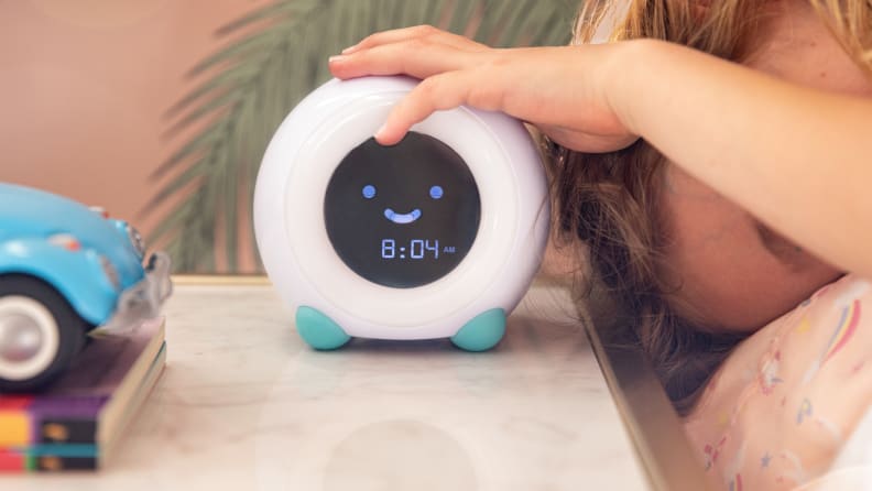 An alarm clock sitting on a bedside table with a child's hand on top.