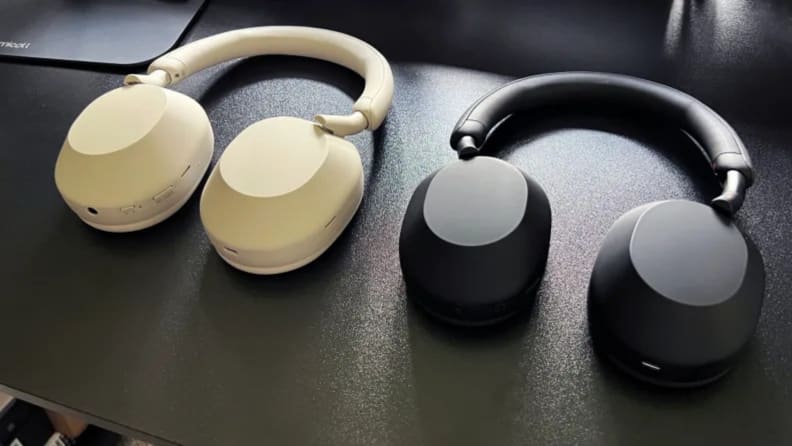 A pair of white headphones next to a pair of black headphones on a table.