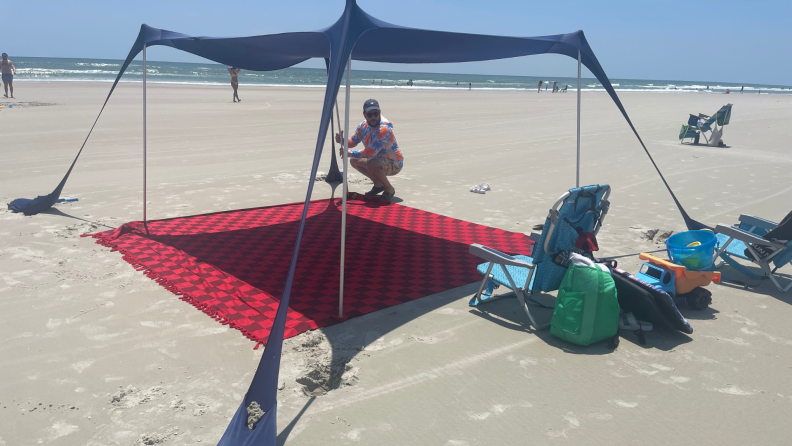 Person propping up sun tent over Big Beachy Blanket on sand outdoors.