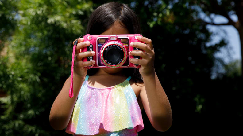 A child holds the VTech KidiZoom in front of their face, taking a photo with it.