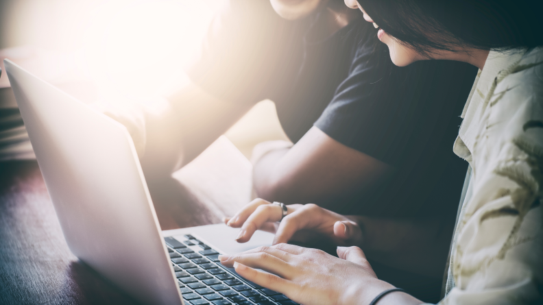 Two people crowd over a computer as if collaborating.