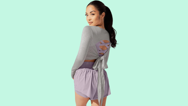 A model wearing purple shorts with a gray top that has cutout and bow details along the back.