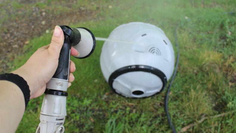 A woman’s hand holding a hose nozzle and spraying the Litter-Robot globe.