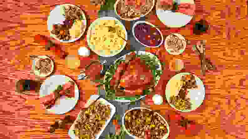 A top-down photo of a Thanksgiving dinner table with four place settings with three people serving themselves from various dishes.