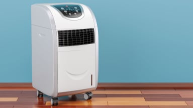A large white portable air conditioner with wheels stands on a wood floor.