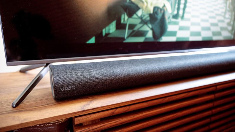 A black soundbar sits on a wooden TV console under a TV.
