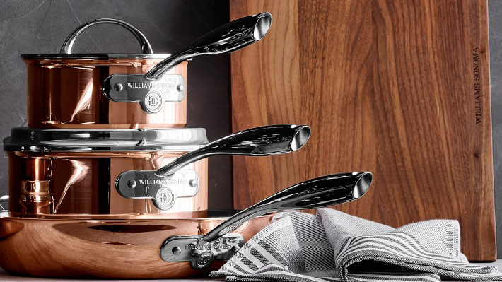 A stack of three copper pots sitting next to a wooden cutting board.