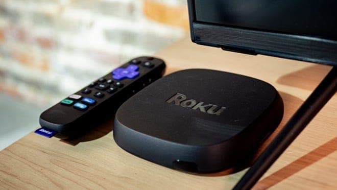 Roku Ultra device and remote sitting on a TV stand next to a TV