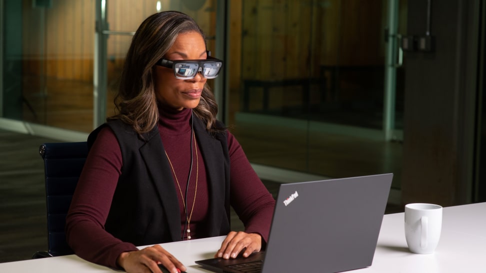 A woman looks at her computer through smart glasses.