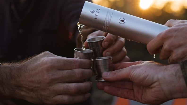 Hands pouring liquid into steel shot glasses.