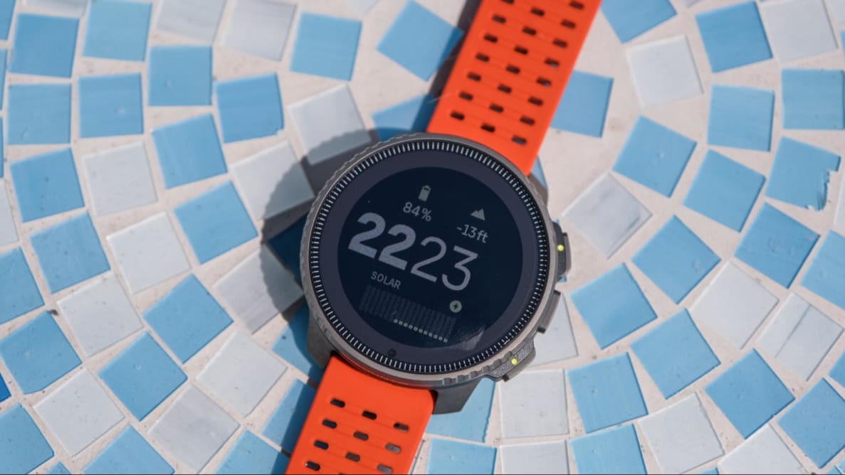 The Suunto Vertical Titanium Solar outdoor watch sits on a blue mosaic tabletop