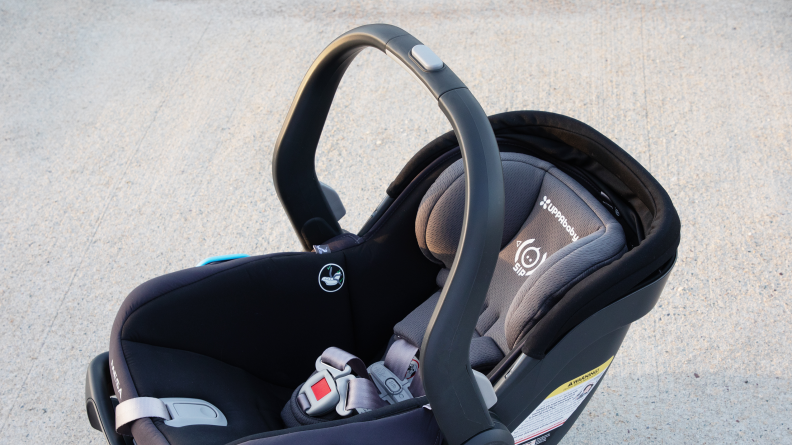 The Uppababy Mesa V2 car seat sitting on the pavement with the handle raised.