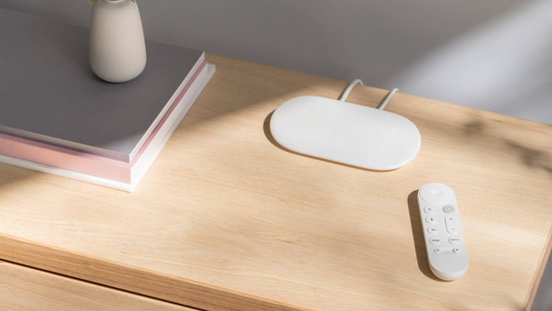 The Google TV Streamer shown in white sitting on a wood table.