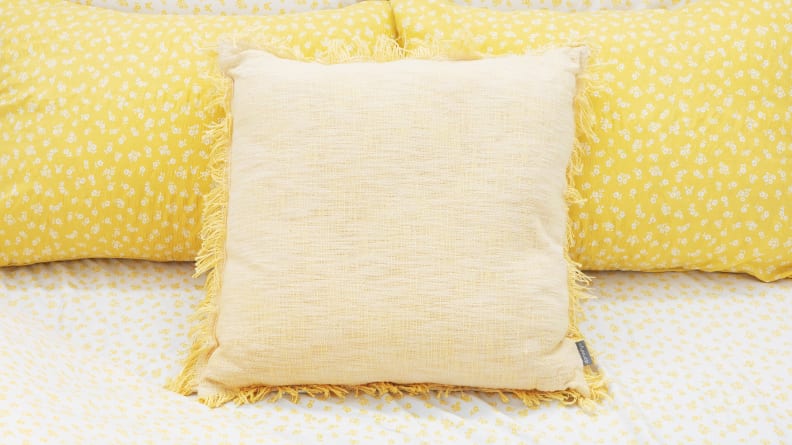 A yellow throw pillow sits on a bed.
