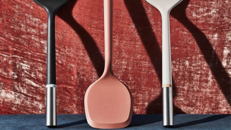 Three colorful spatulas propped against a wall arranged in a row.