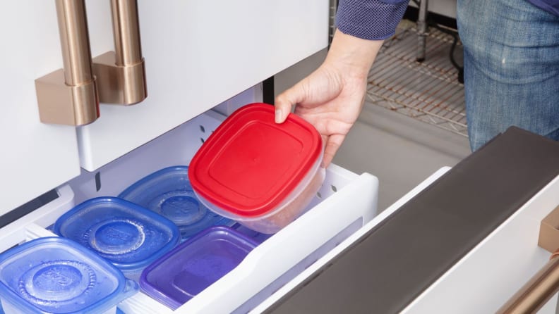 Lab technician placing ballast container inside of freezer drawer on refrigerator.
