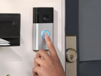 A person’s finger presses the chime button on the new Ring Battery Doorbell that is hanging on the exterior of a home