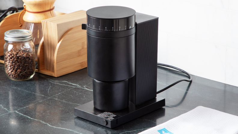 Shot of the Fellow Opus coffee grinder on countertop next to jar of coffee beans.