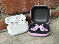 The Apple AirPods Pro 2 and Beats Fit Pro side by side on concrete steps with a brick wall in the background.