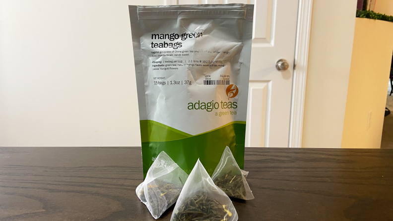 Table with a bag of Adaigo green tea sitting on top. Three small tea bags sit outside the main bag.