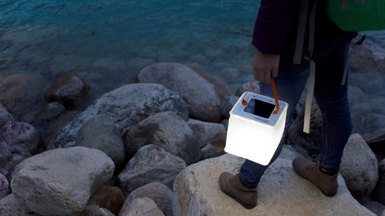 Person holiding glowing lantern standing on rocks