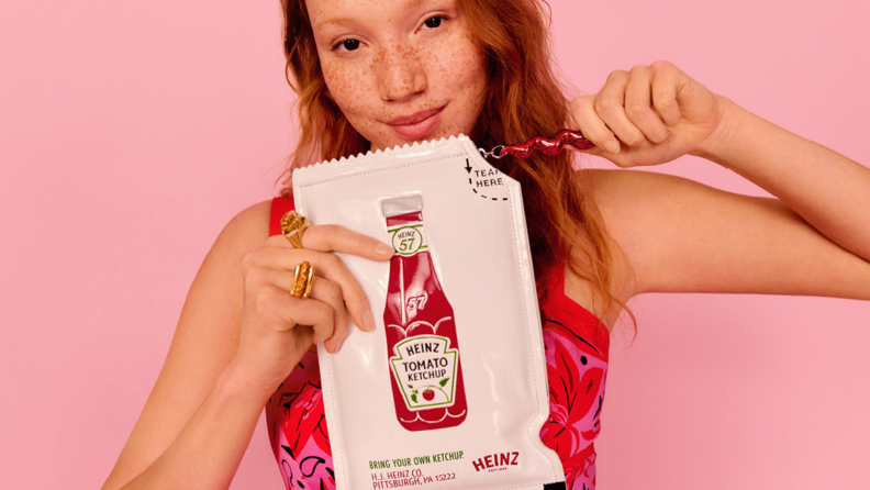 A model holding a Kate Spade New York clutch that looks like an oversized Heinz Ketchup packet.