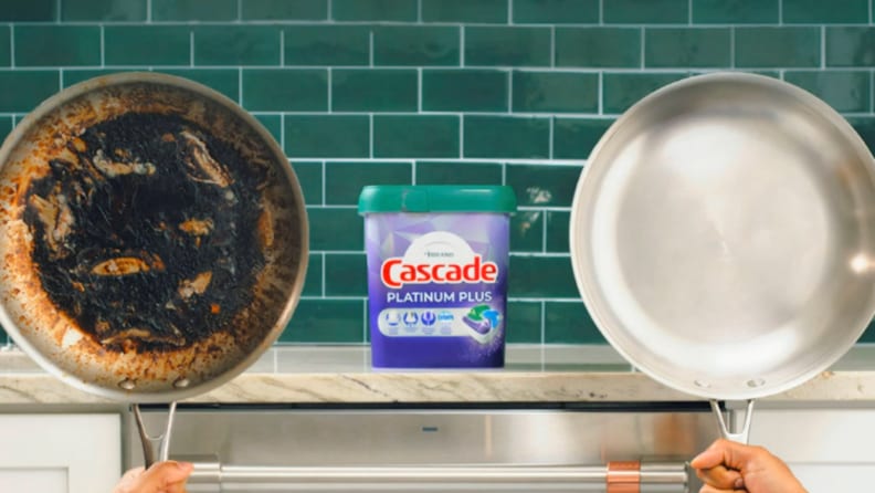A greased pan on the left and a clean pan on the right, with Cascade dishwasher pod in the middle, on top of a kitchen counter with a green backsplash