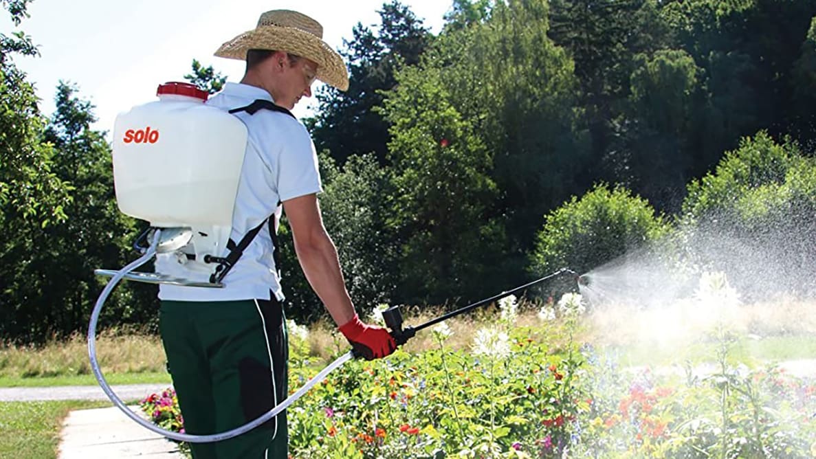 一个带着背包喷雾器在花园治疗的人。