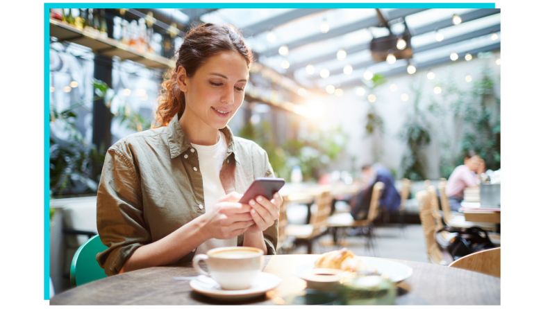 Person sitting at restaurant checking phone in front of cup of coffee.