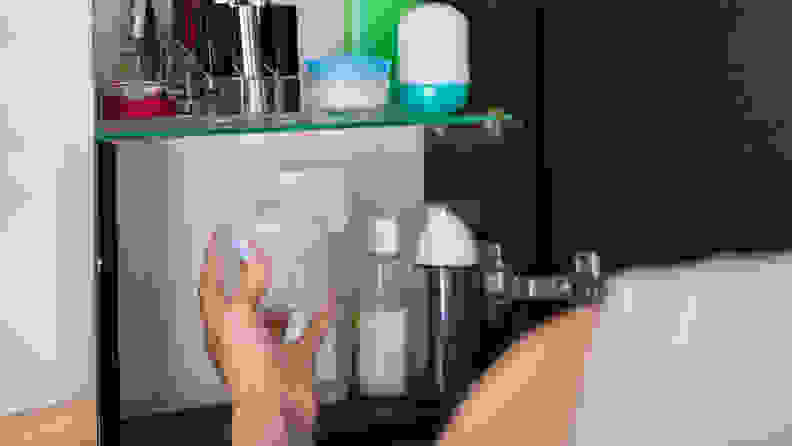 A person's hand reaching into a medicine cabinet to grab a jar.