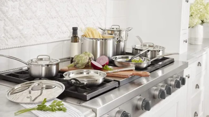 Lifestyle image of the 12-piece Cuisinart stainless steel cookware set spread out on a stove and kitchen countertop.