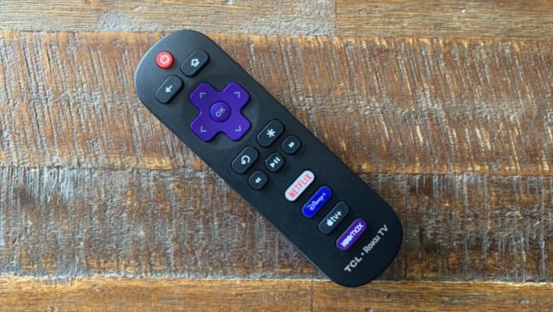 The Roku remote for a TCL 5-Series TV sittingon a wooden table.