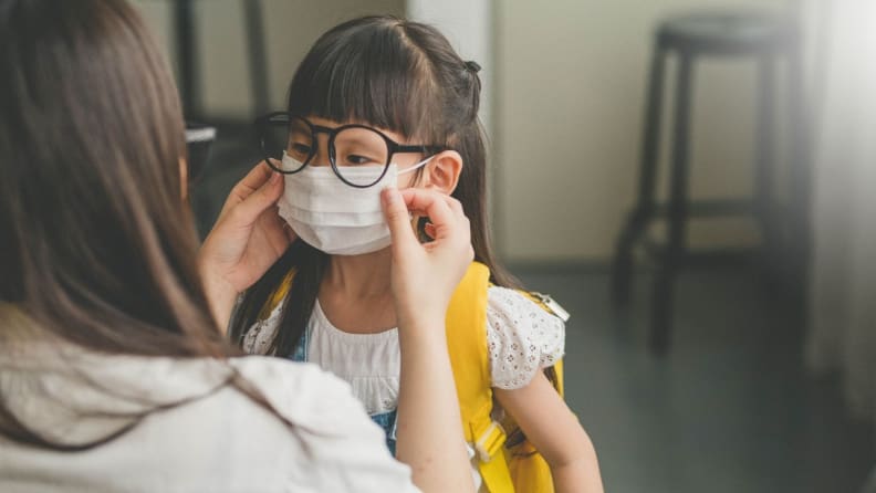 A parent places a surgical mask on a child's face.