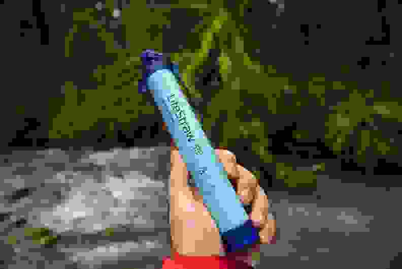Hand holding a lifestraw water filter in front of a creek