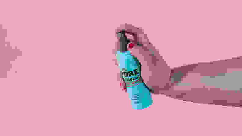 A person's hand spraying a makeup setting spray.