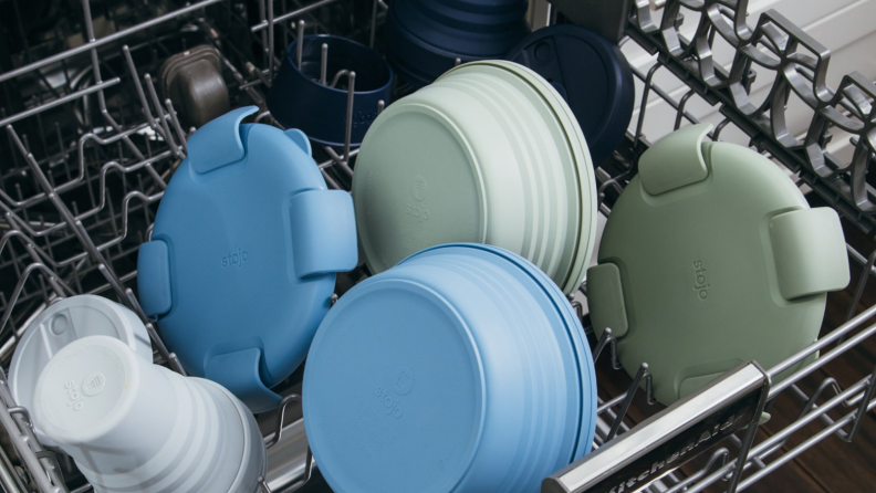 On the top rack of a dishwasher, there are some Stojo products.