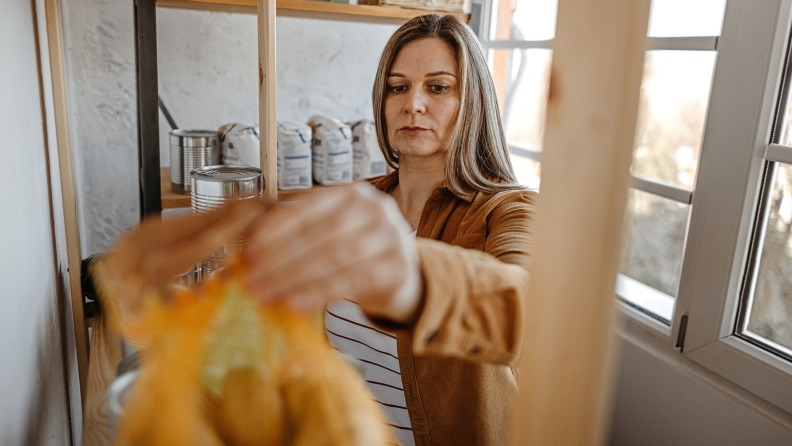 A person takes a bag of goods off a pantry shelf.