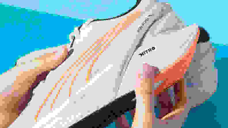 A person grips the underside of a white running shoe.