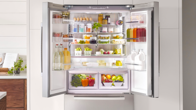 A Bosch refrigerator with doors wide open, revealing shelves full of groceries.