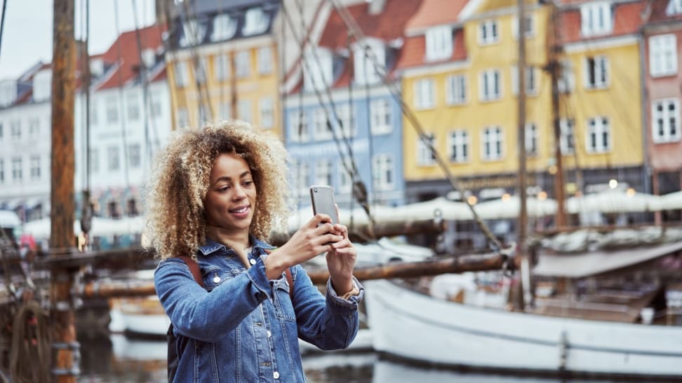 A woman in a denim jacket takes a photo of a canal with her smartphone