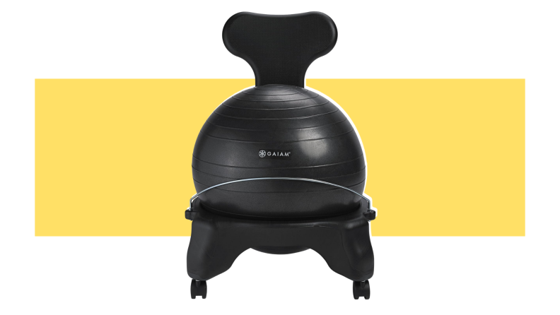 Black yoga ball sitting inside of black seat frame in front of yellow background.