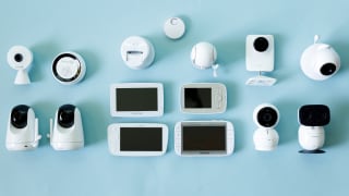 Many baby monitors with video screens lay on an aqua background