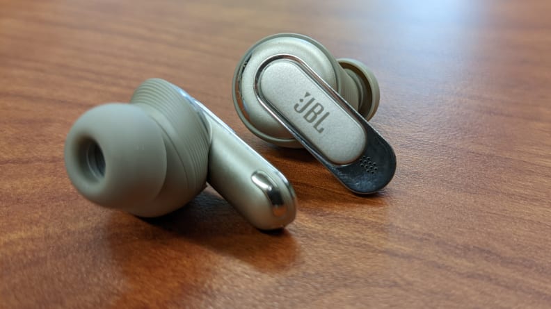 The JBL Tour Pro 2 earbuds sitting on a wooden table.