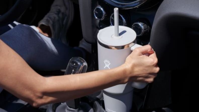 A white woman's arm grips a travel mug in a car's cup holder