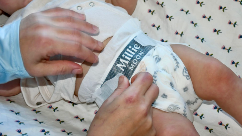 A person putting Millie Moon diapers on a child.