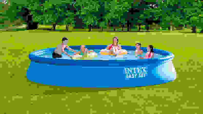 A family lounging in an inflatable above-ground swimming pool set up in their backyard.