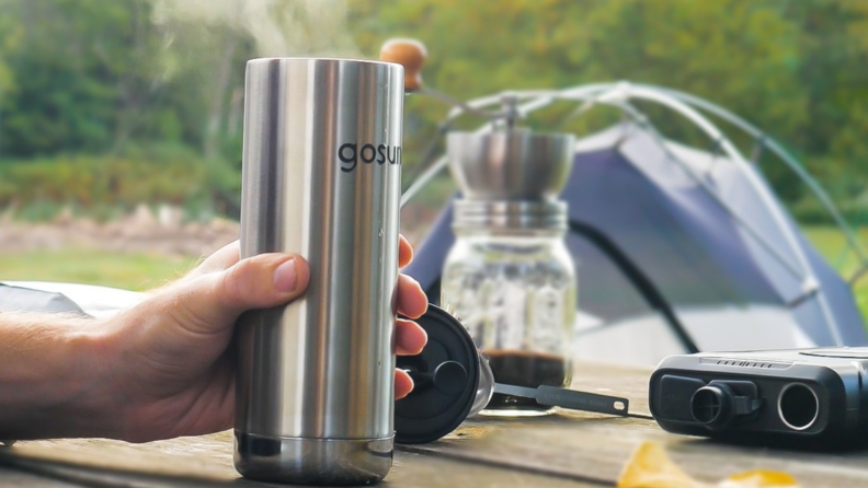 A person is holding a GoSun coffee maker at what appears to be a campsite. There's a tent in the background.