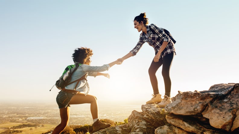 One woman lending another woman a hand while climbing up a mountain.